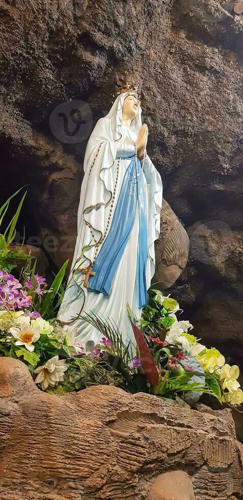 estatua de santo Virgen María en romano católico iglesia, en el cueva de Virgen María, en un rock cueva capilla católico Iglesia con tropical flores alrededor foto