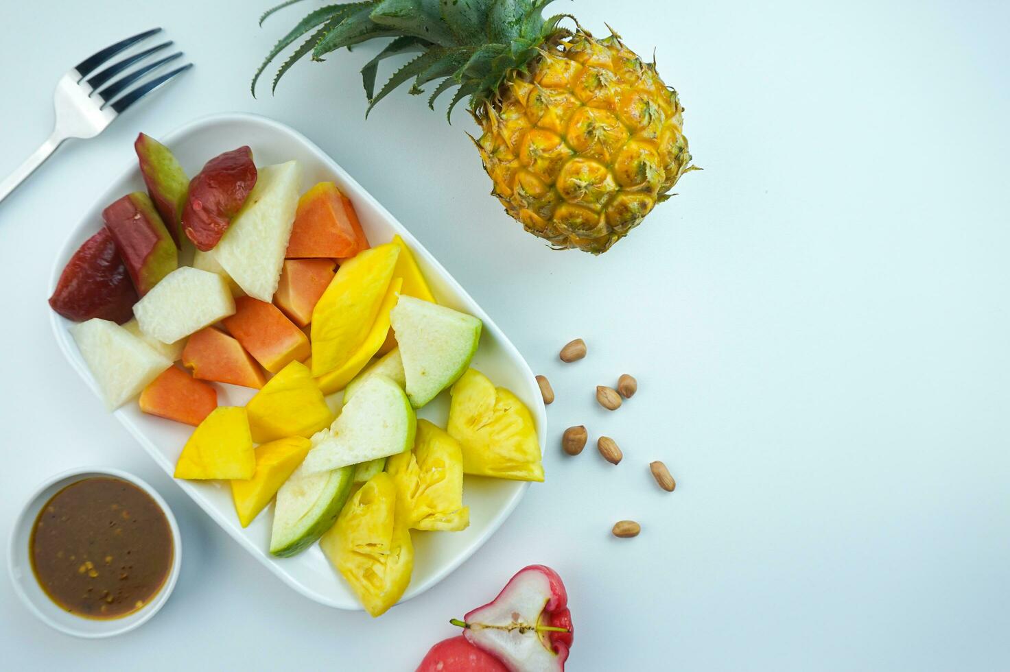 Sliced Fruit Salad, in Indonesia known as Rujak Buah or Lutis or Lotis. Served with Spicy Brown Sugar sauce and Ground Peanuts in a plate on white background photo