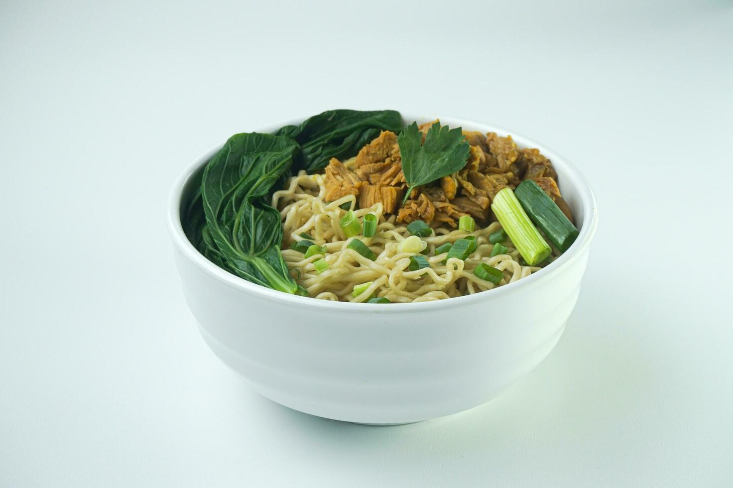 Noodles with Chicken, in Indonesia it is known as Mie Ayam. Served with green vegetable chili sauce in a bowl on white background by hand photo