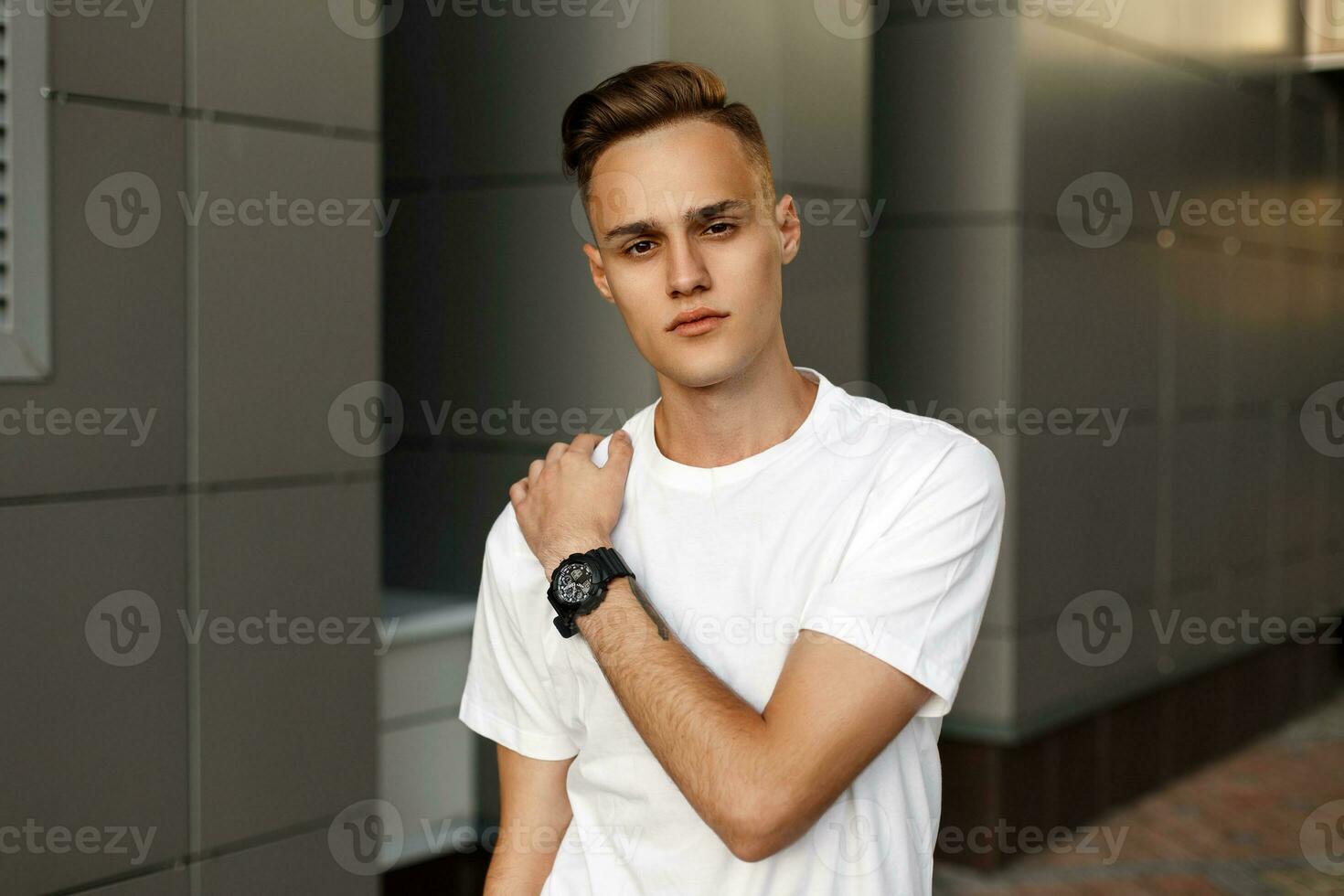 Young handsome guy in a white T-shirt posing near modern gray wall. photo