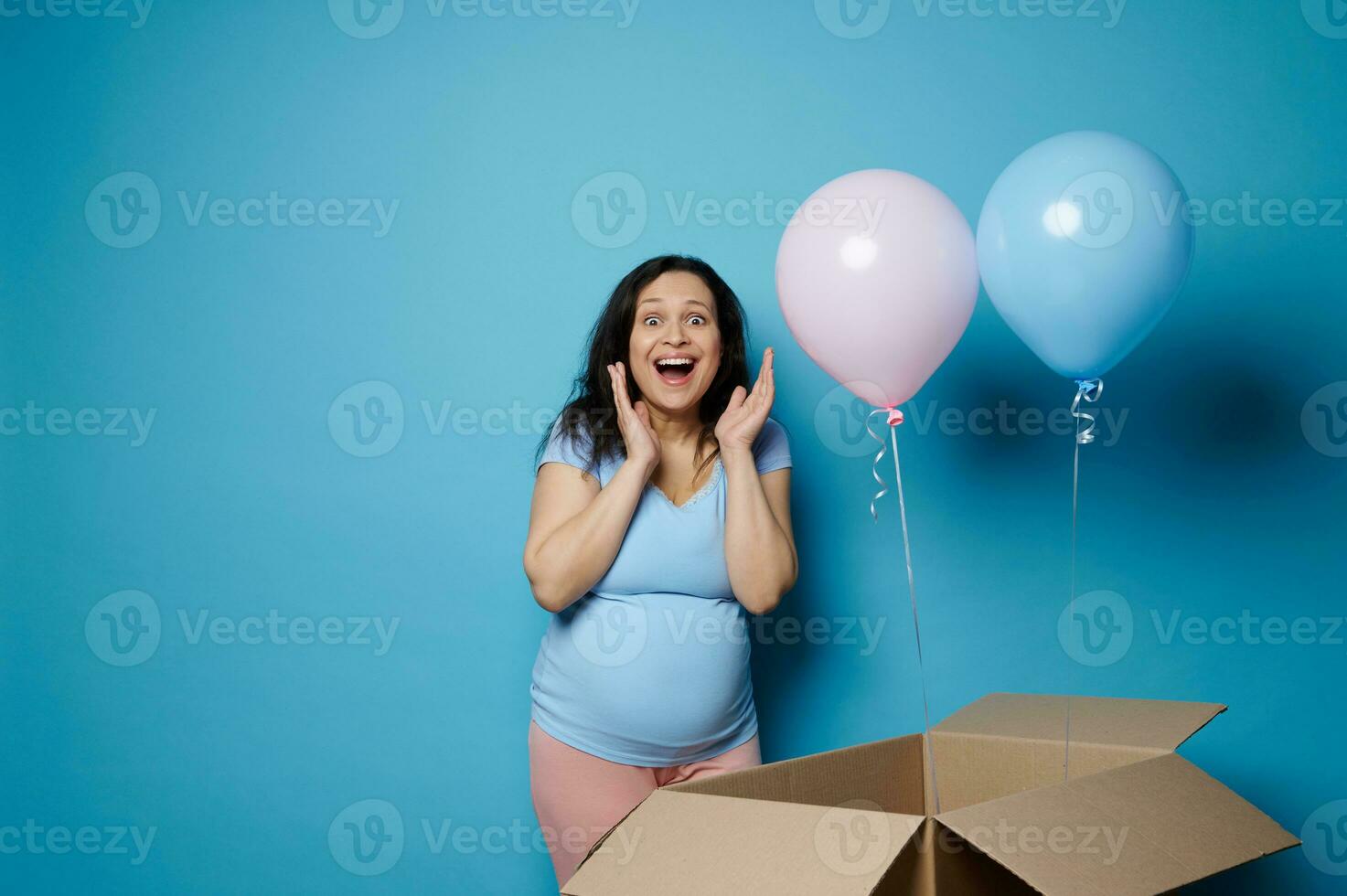asombrado contento embarazada mujer expresando sorpresa a género revelar fiesta, esperando Gemelos bebé chico y chica, azul fondo foto