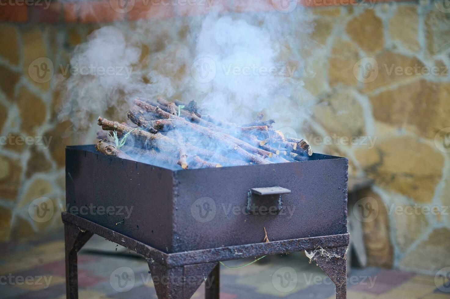 Cose-up view of a smoke coming from a hot barbecue fire with burning tree branches over a black grill in the backyard photo