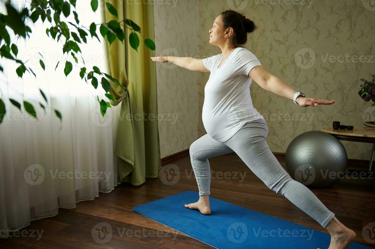 embarazada mujer practicando yoga, en pie en aptitud estera en guerrero pose, disfrutando sano estilo de vida durante su el embarazo foto