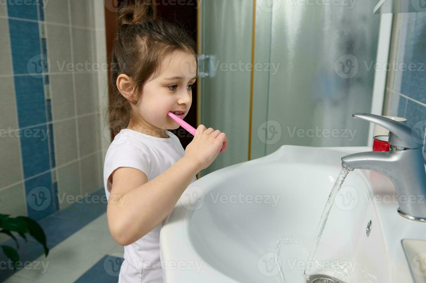 hermosa preescolar pequeño niña cepillado dientes, en pie por lavabo en el hogar baño. dental cuidado y oral higiene. foto