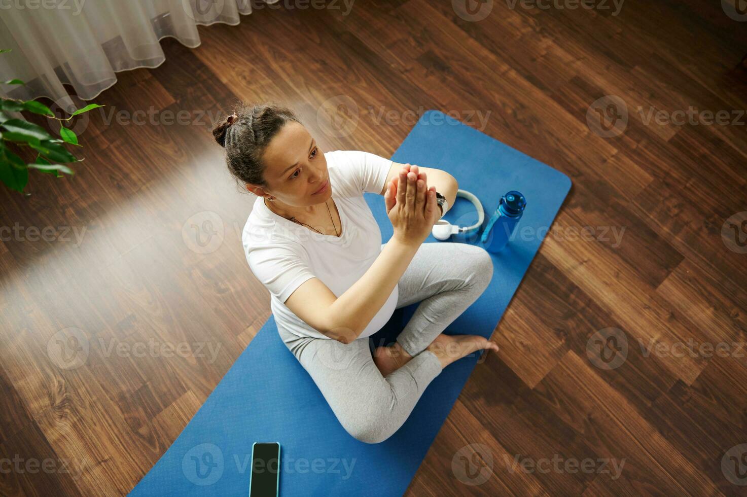 Pregnant expectant woman exercising yoga, breathing exercises and prenatal stretching, sitting in lotus posture on a mat photo