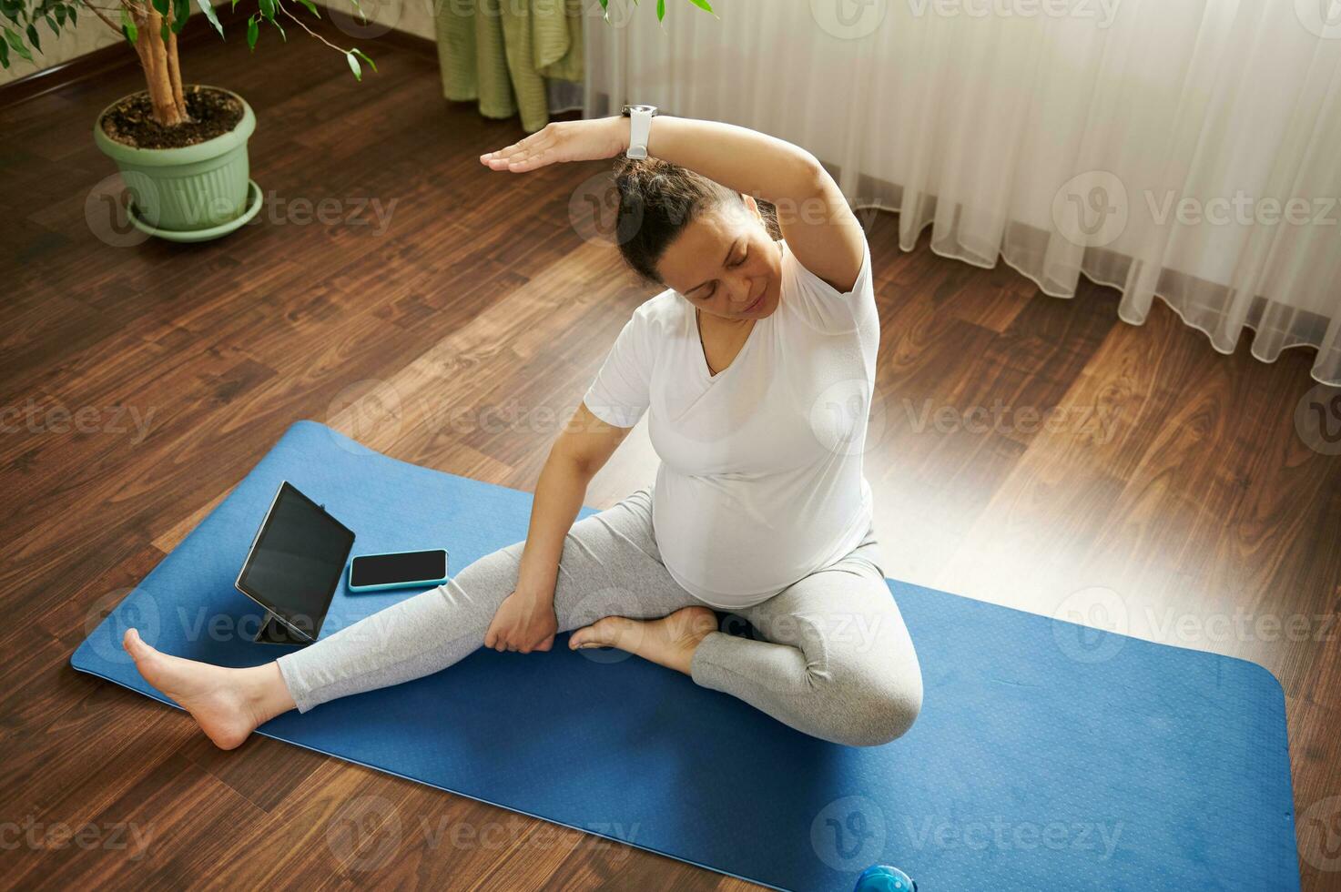 Pregnant woman practicing online pregnancy yoga on a mat, doing prenatal stretching in body balance exercise. Top view photo