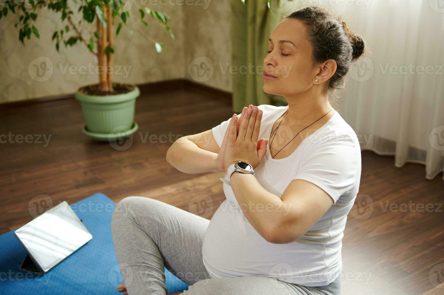 maravilloso embarazada mujer mantiene manos palmas juntos, haciendo el embarazo yoga y aliento ejercicios a hogar. en línea yoga clase foto