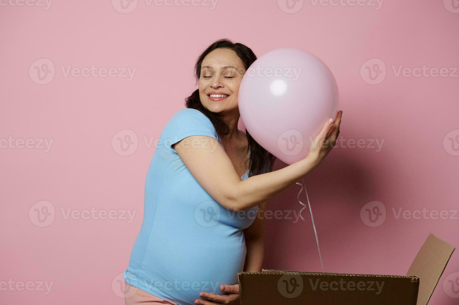 Delightful conscious pregnant woman gently hugging pink balloon, feeling happy positive emotions expecting a baby girl, photo