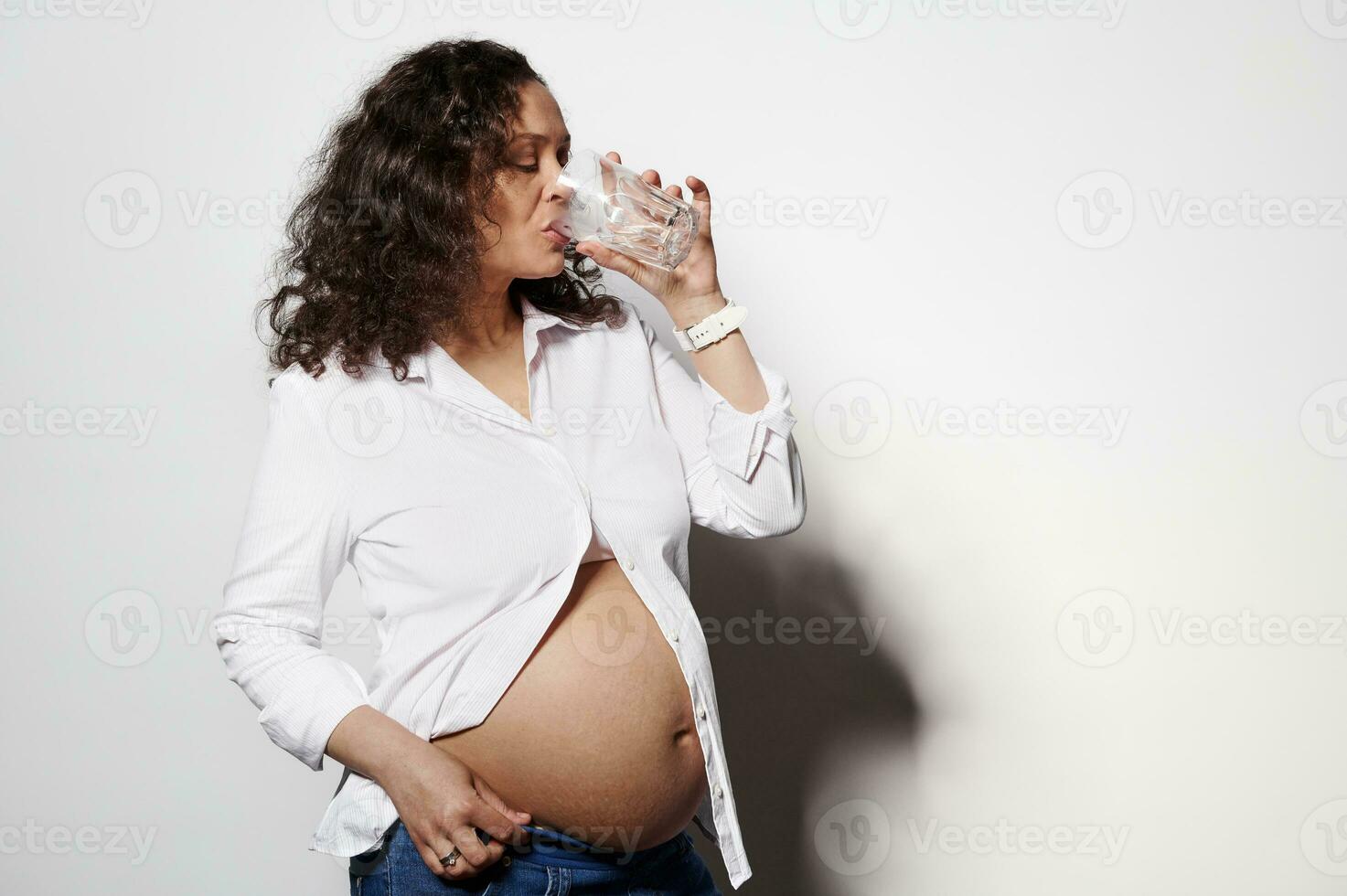 Conscious adult pregnant woman taking medicines and nutritional supplement, drinking water, isolated on white background photo