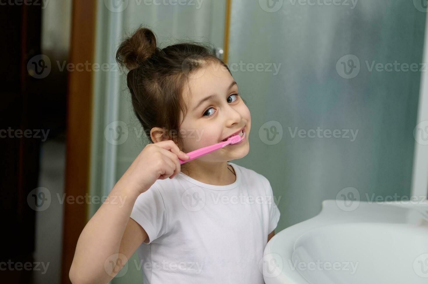 Dental care and oral hygiene for healthy white baby teeth. Close-up smiling child girl brushing teeth looking at camera. photo