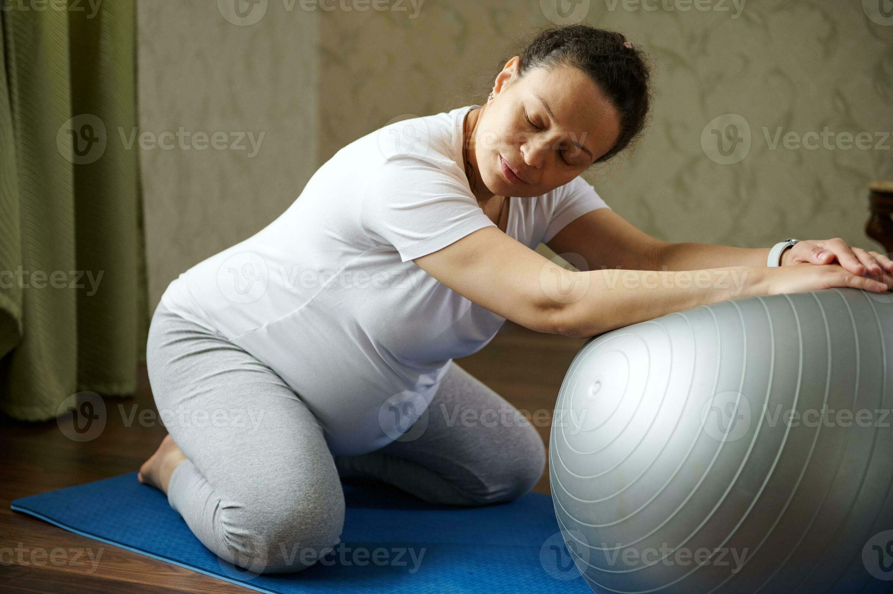 Pregnant woman exercising with fit ball, practicing pregnancy yoga