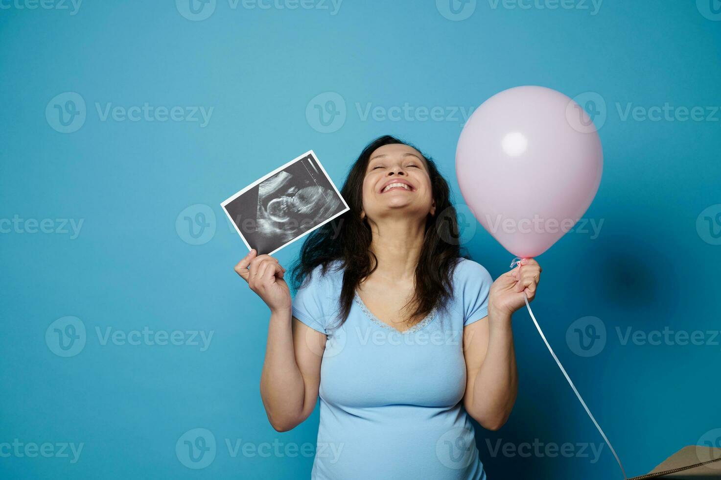 lleno de alegría embarazada mujer expresando positivo emociones esperando bebé chica, posando con rosado globo y ultrasonido escanear foto