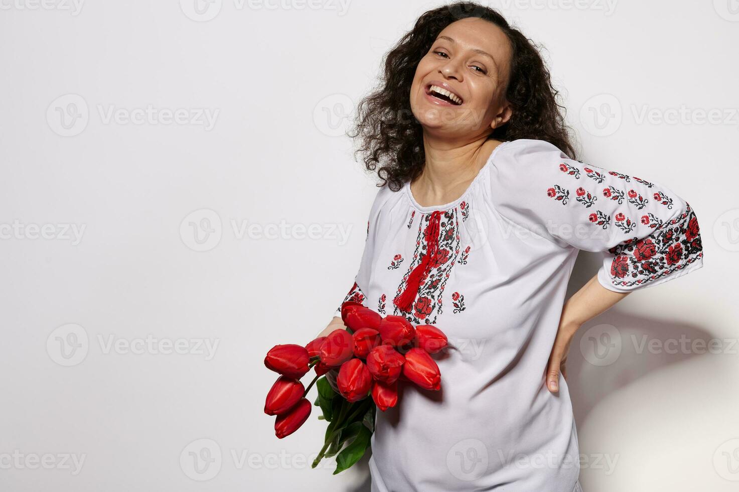 Smiling laughing happy young pregnant woman in embroidered ethnic Ukrainian dress, with beautiful bouquet of red tulips photo