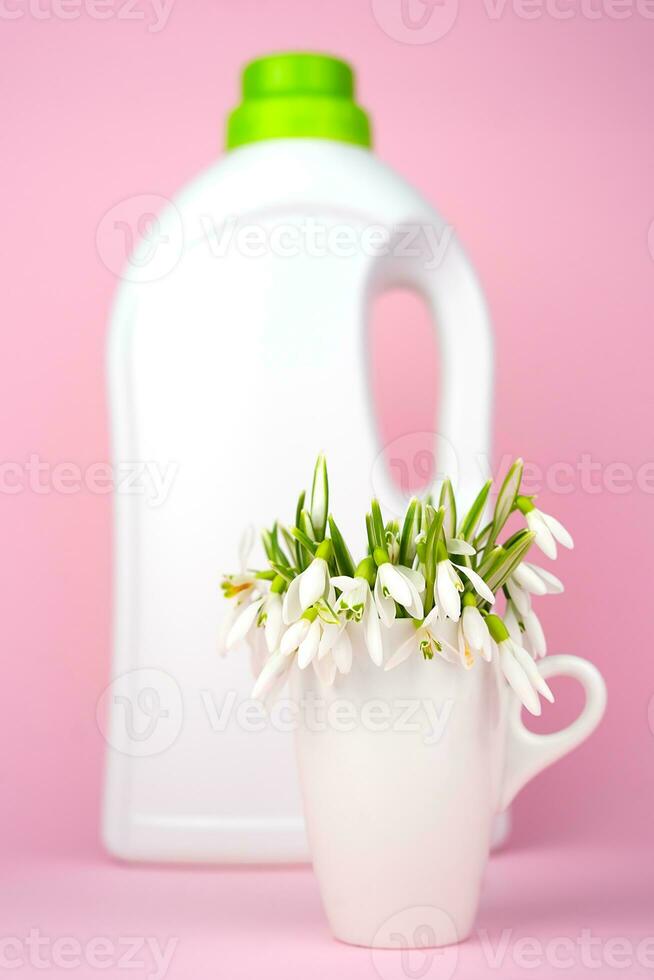 A spring flowers and bottle of liquid laundry detergent on a pink background. Washing and cleaning concept. Close-up. Selective focus. photo