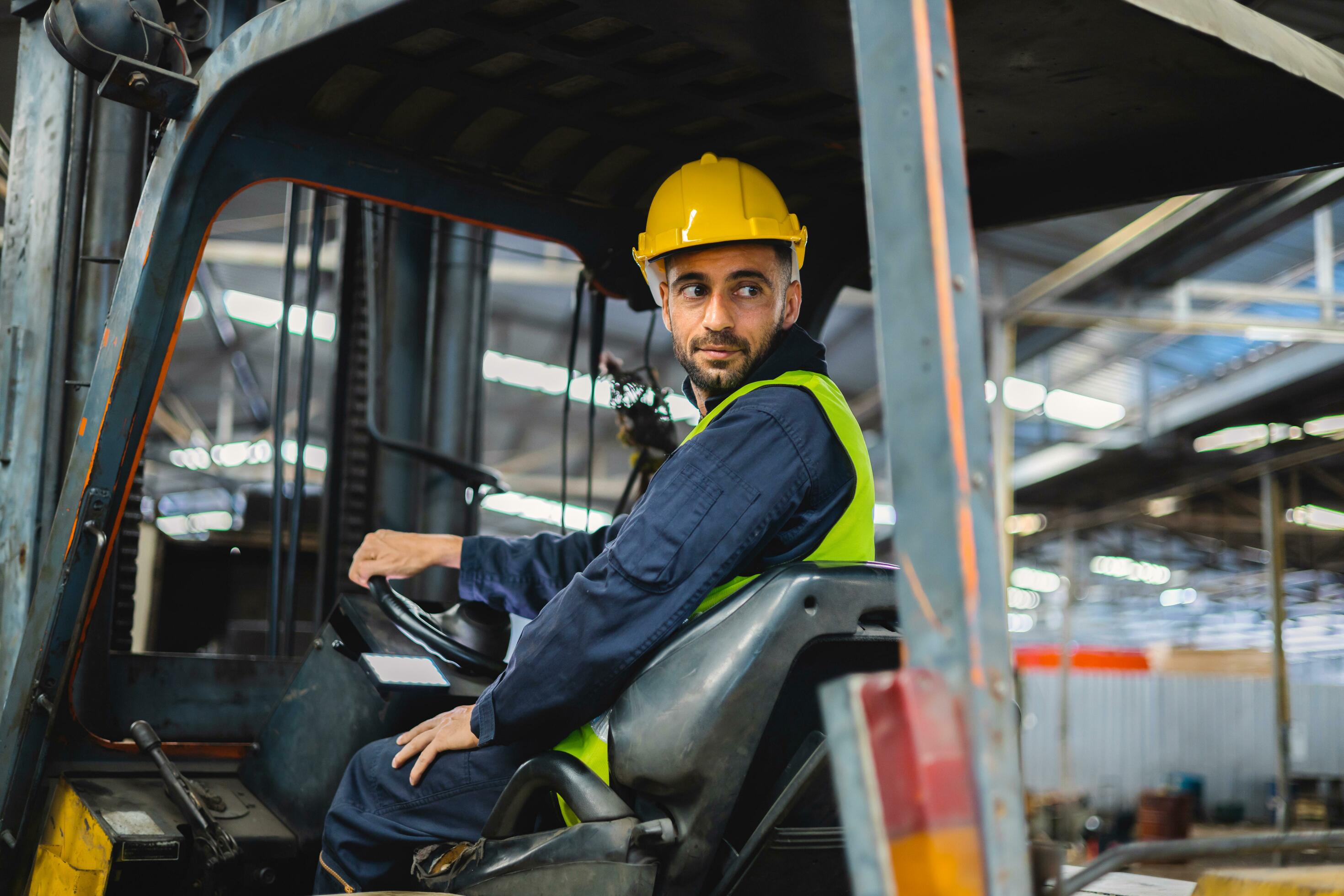 worker wearing helmet with driving forklift backwards in warehouse