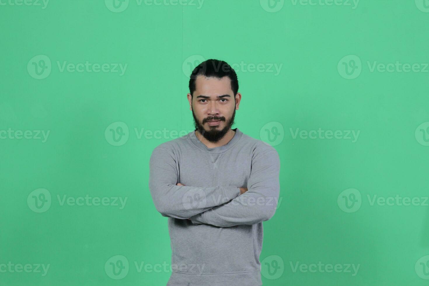 barbado asiático hombre poses vistiendo un gris camisa en contra un verde antecedentes foto