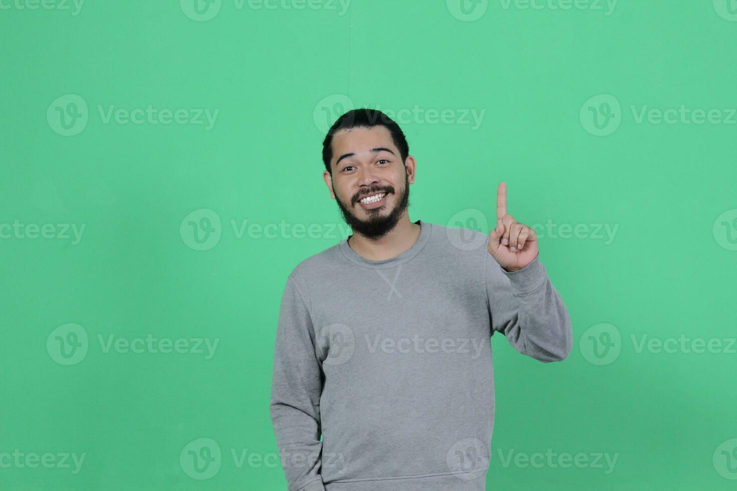 barbado asiático hombre poses vistiendo un gris camisa en contra un verde antecedentes foto