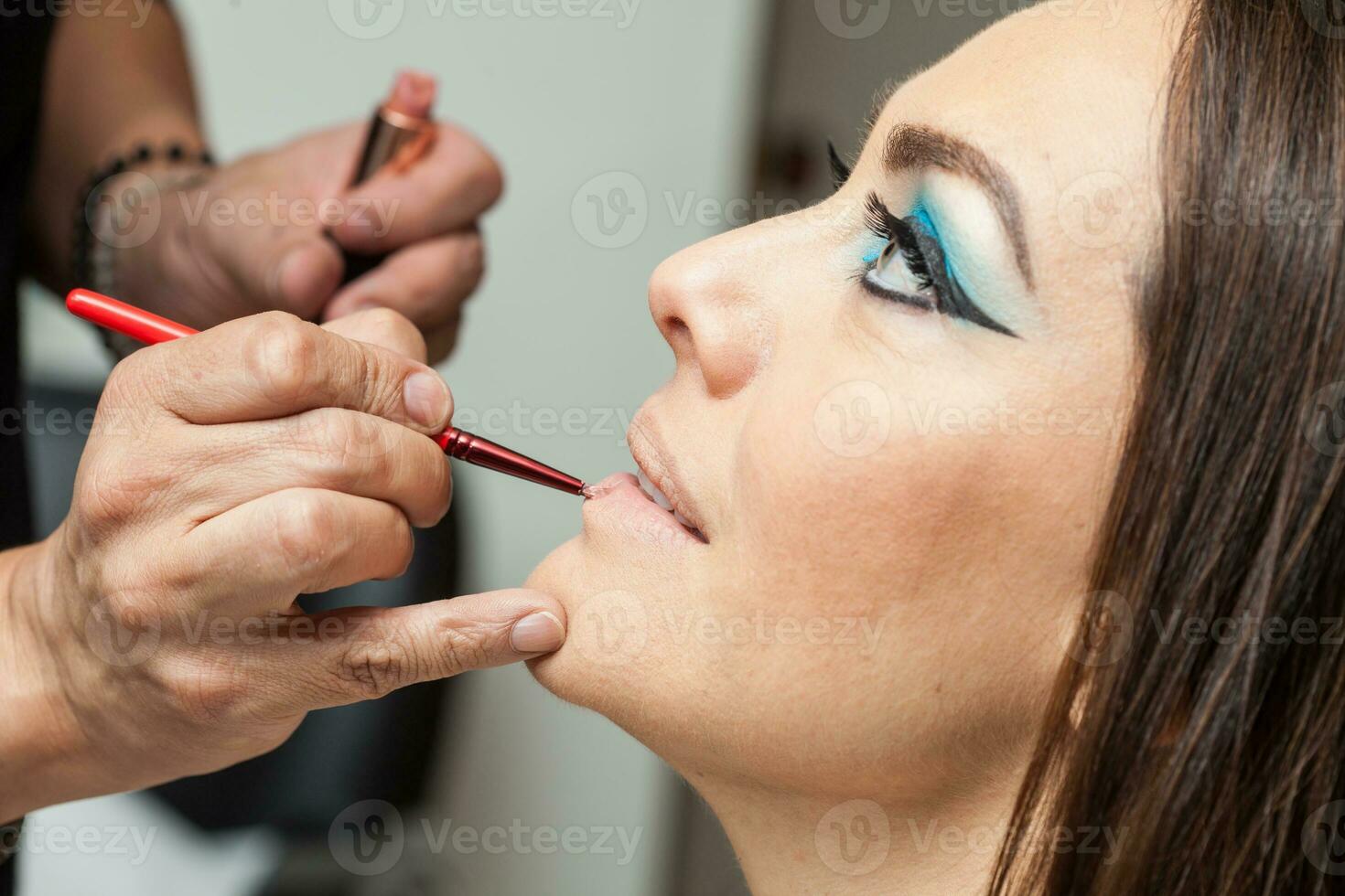 Makeup artist applying lipstick to a white woman photo