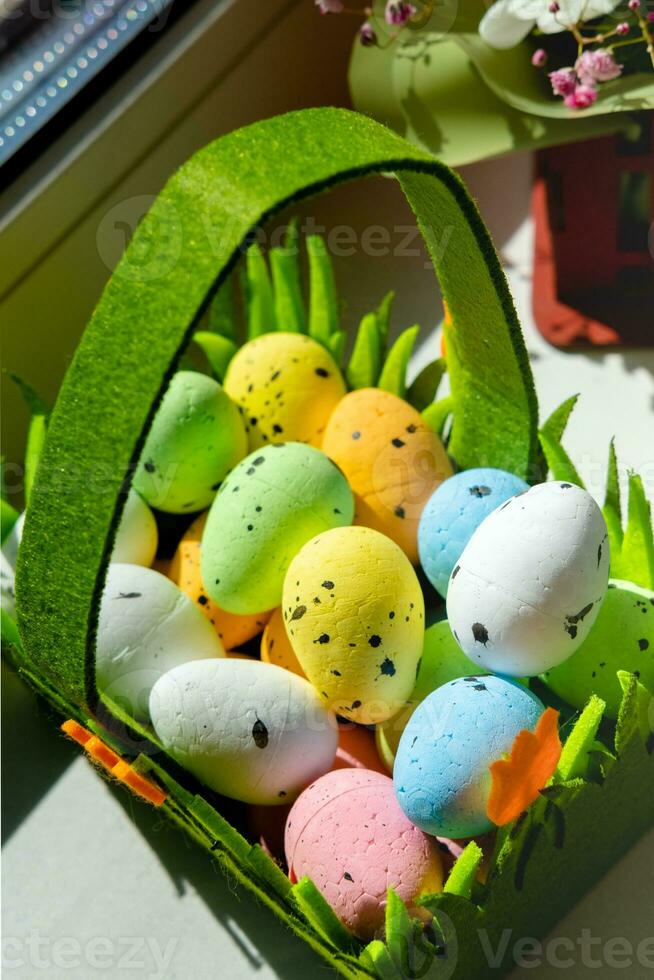 Easter green basket with plastic colored eggs on the windowsill photo