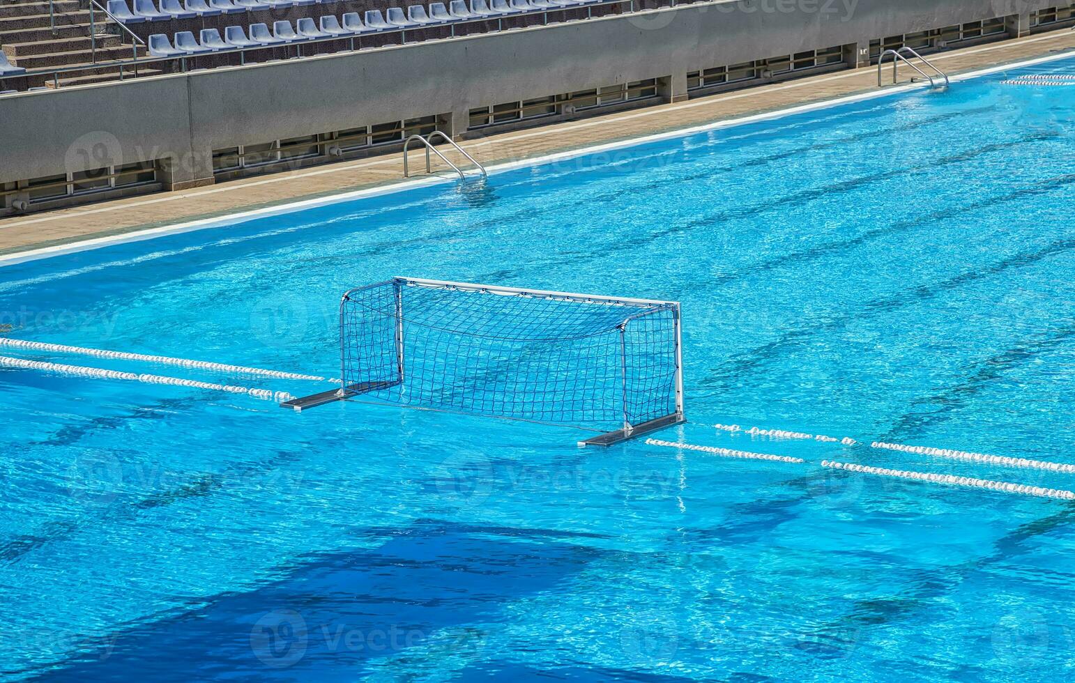 Empty water polo goal. Water sports equipment. Water polo goal with white frame and net supported with rope and floating buoys resting on the swimming pool. photo