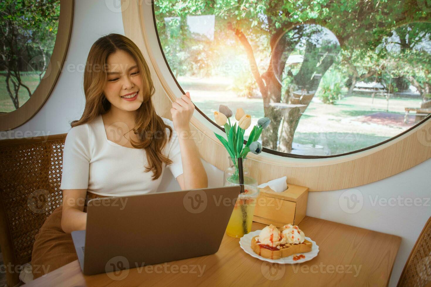 Young smart asian woman freelance online working from cafe with Laptop computer. Young beautiful joyful female smiling while working, thinking about how to take the business to technological heights. photo