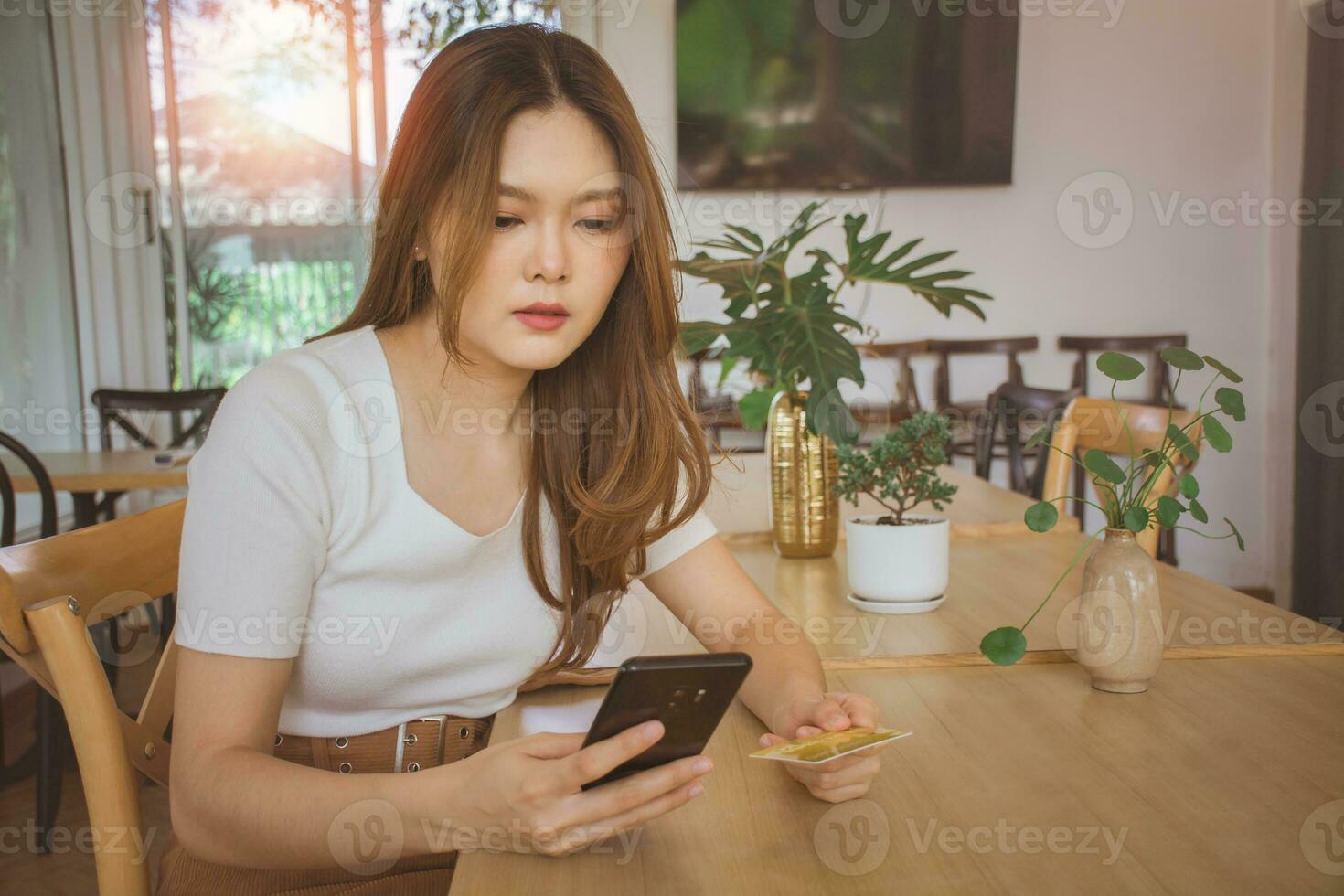 Young woman using credit card and mobile phone for online shopping in cafe, coworking space or coffee shop. Technology money wallet, online payment concept, credit card mockup. Safe mobile banking photo