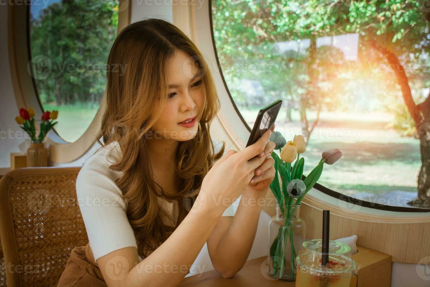 Young adult happy asian woman using smart phone for social media application, shopping online, transfer money, financial, message in cafe. Background with window and warm sunlight on winter season. photo