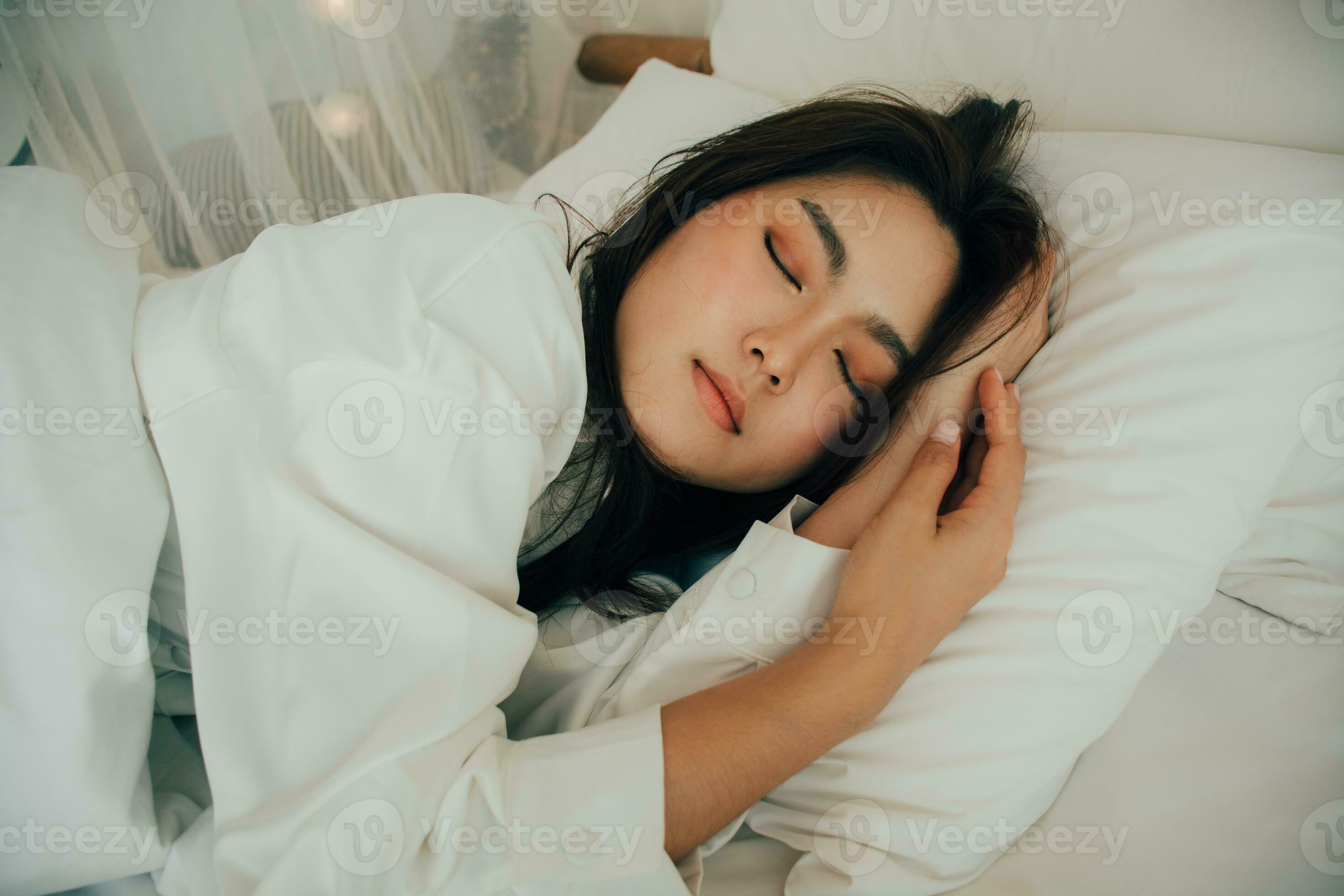 Young woman sleeping in bed, her head resting on a white pillow with