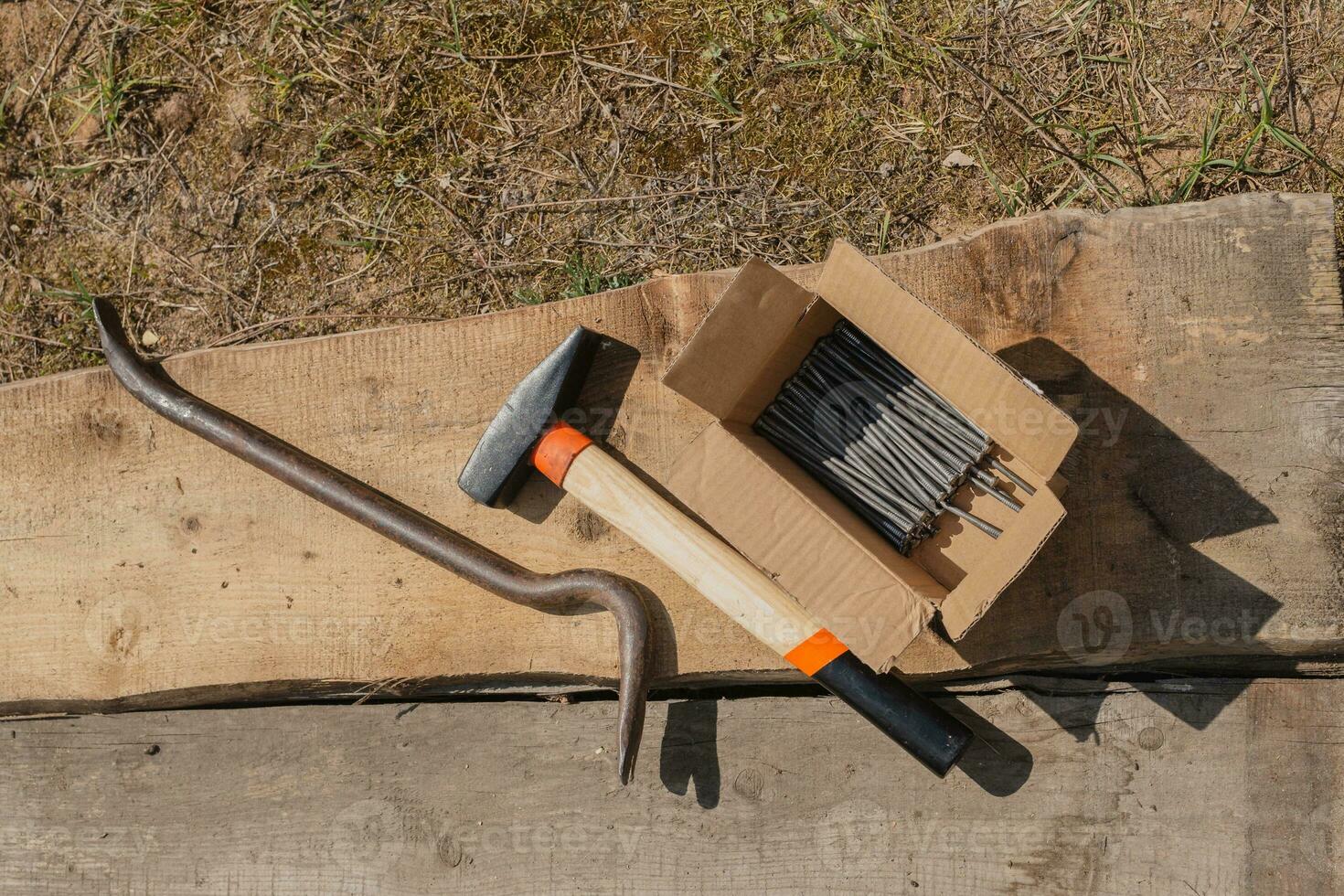 Workplace of a carpenter in the yard - hammer, nails and pry bar next to planks on the ground - nail puller photo