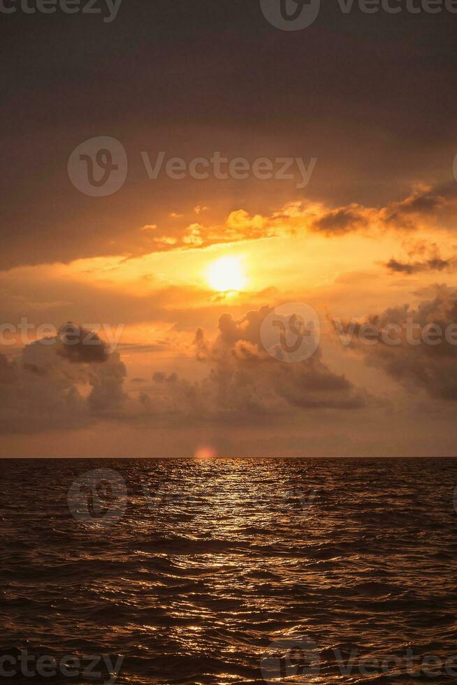 brillante ardiente vistoso mar puesta de sol - nublado cielo y ondas en el agua - vertical hermosa paisaje a puesta de sol en amarillo rojo y naranja colores foto