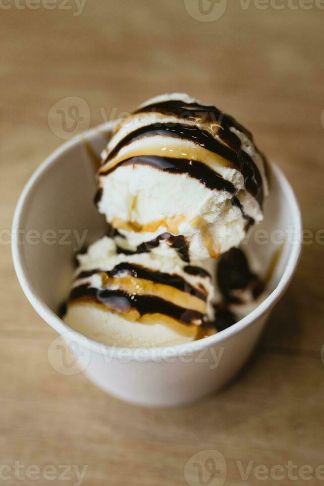 Balls of creamy ice cream in a cardboard cup with chocolate caramel topping photo