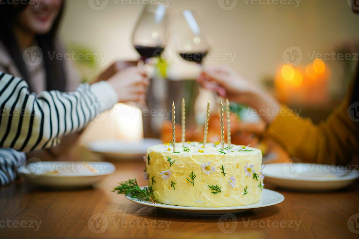 Cheerful friends enjoying home Birthday holiday party. Asian sister cheering drinking red wine celebrating with Birthday cake photo