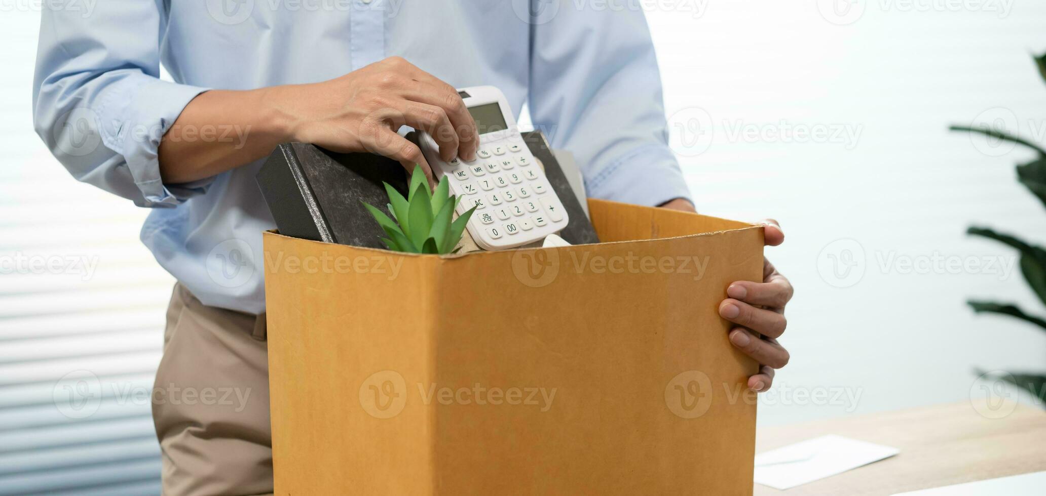 Business man sending resignation letter and packing Stuff Resign Depress or carrying business cardboard box by desk in office. Change of job or fired from company photo