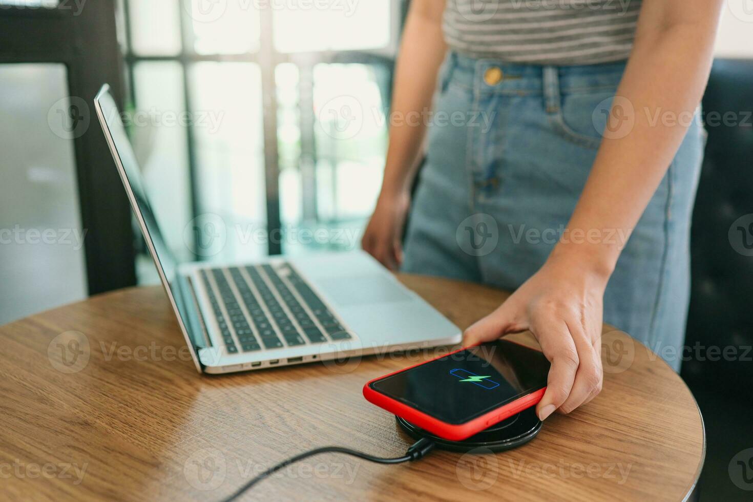 Charging mobile phone battery with wireless charging device in the table. Smartphone charging on a charging pad. Mobile phone near wireless charger Modern lifestyle concept. photo
