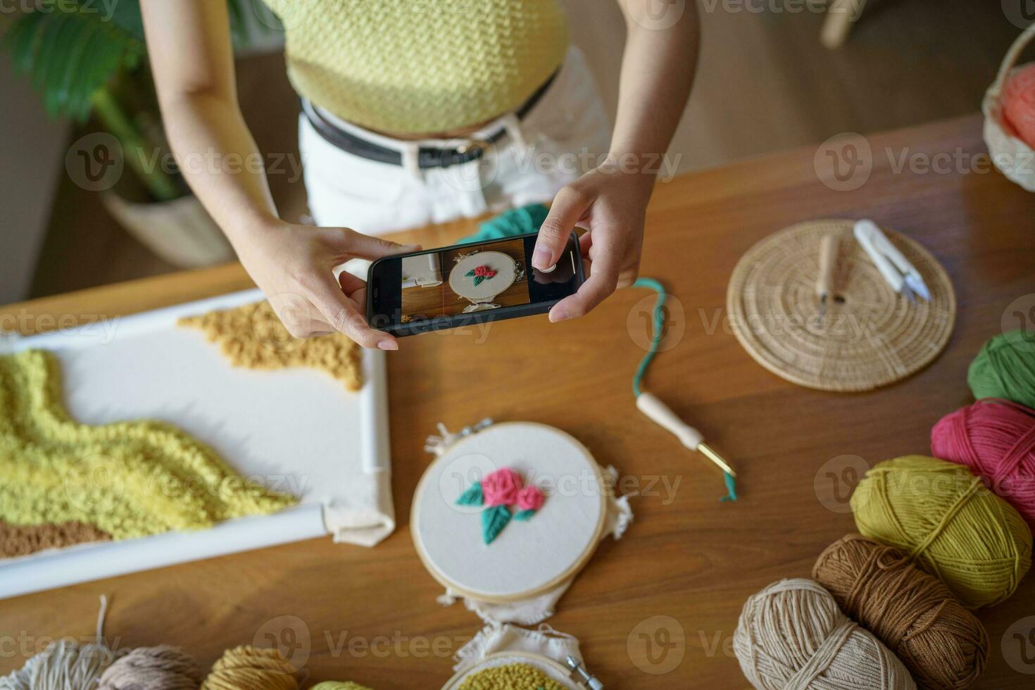 asiático mujer tomando teléfono inteligente foto puñetazo aguja. teléfono destino en social redes en estudio taller. diseñador lugar de trabajo hecho a mano arte proyecto bricolaje bordado