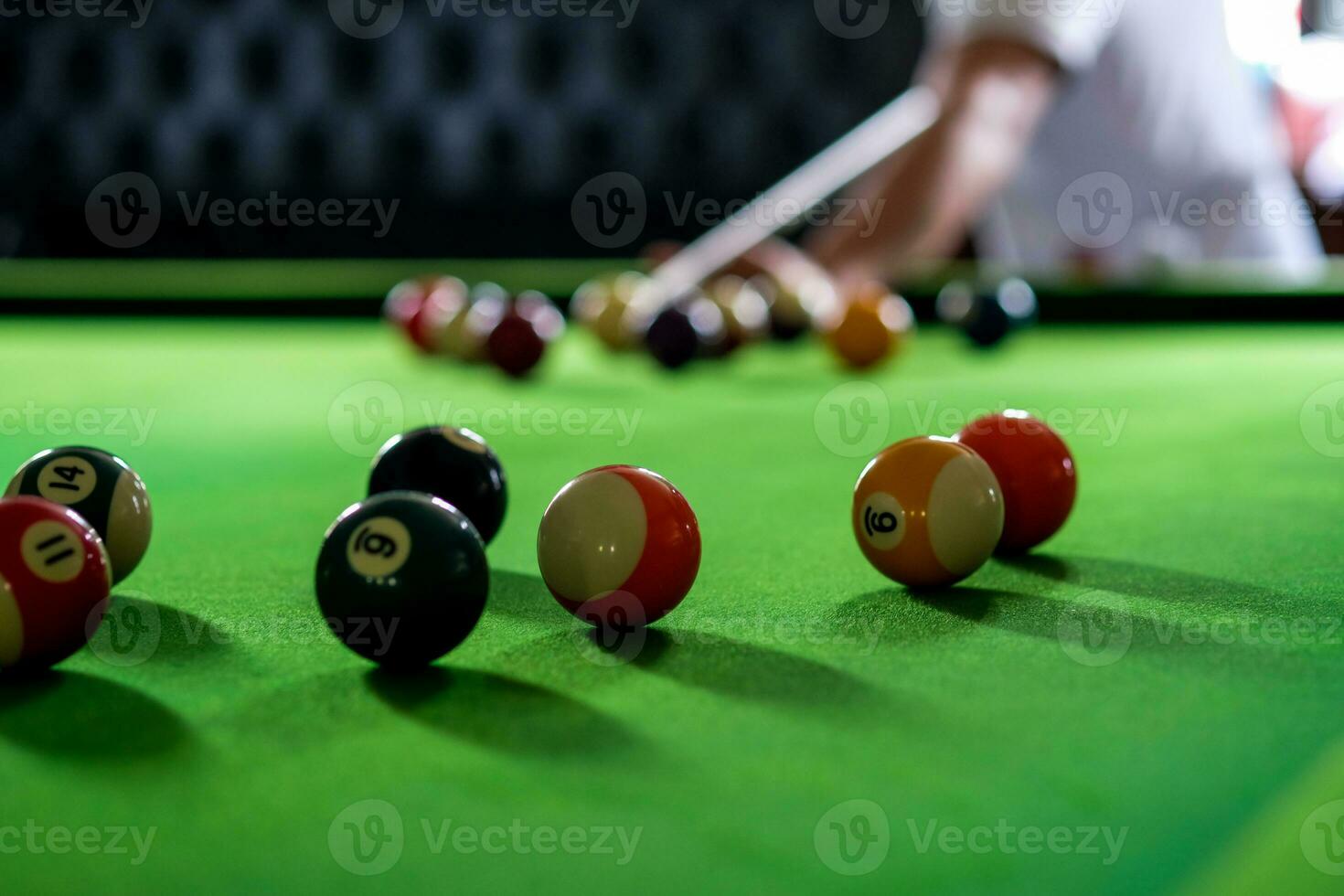 Man's hand and Cue arm playing snooker game or preparing aiming to shoot pool balls on a green billiard table. Colorful snooker balls on green frieze. photo