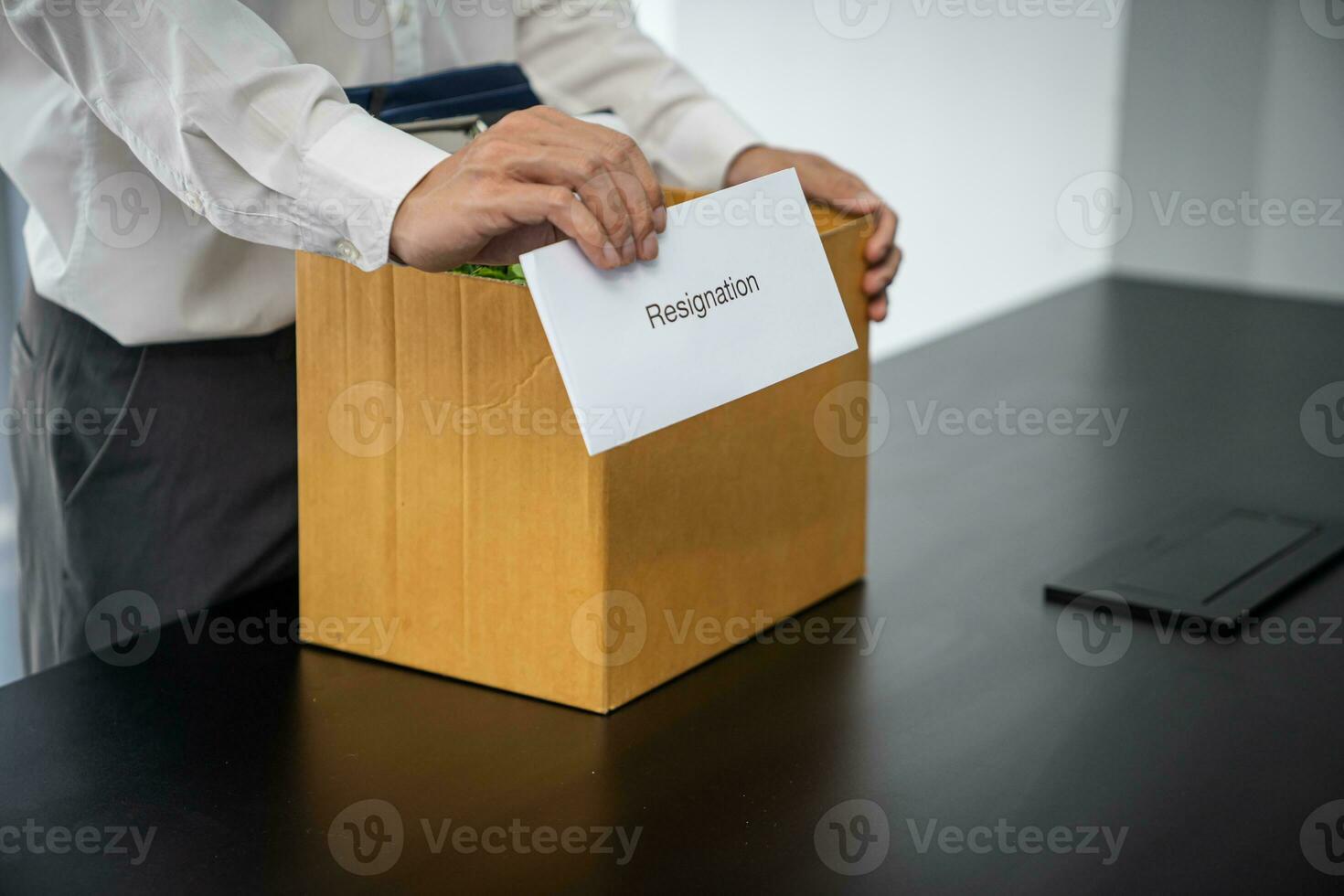 Business man sending resignation letter and packing Stuff Resign Depress or carrying business cardboard box by desk in office. Change of job or fired from company photo