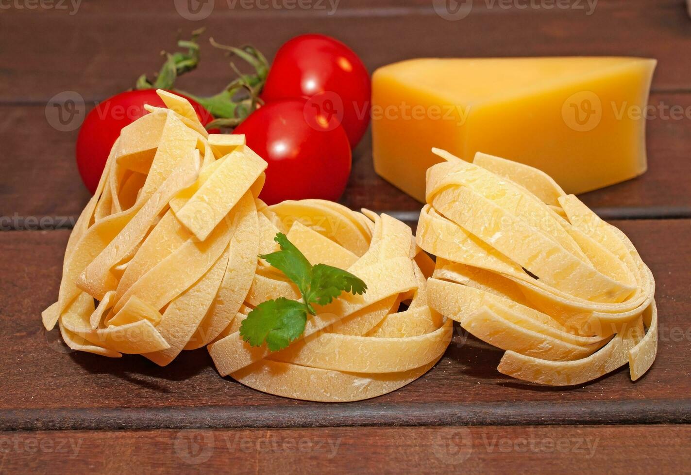 Dry nest pasta on a wooden table with tomatoes and cheese photo