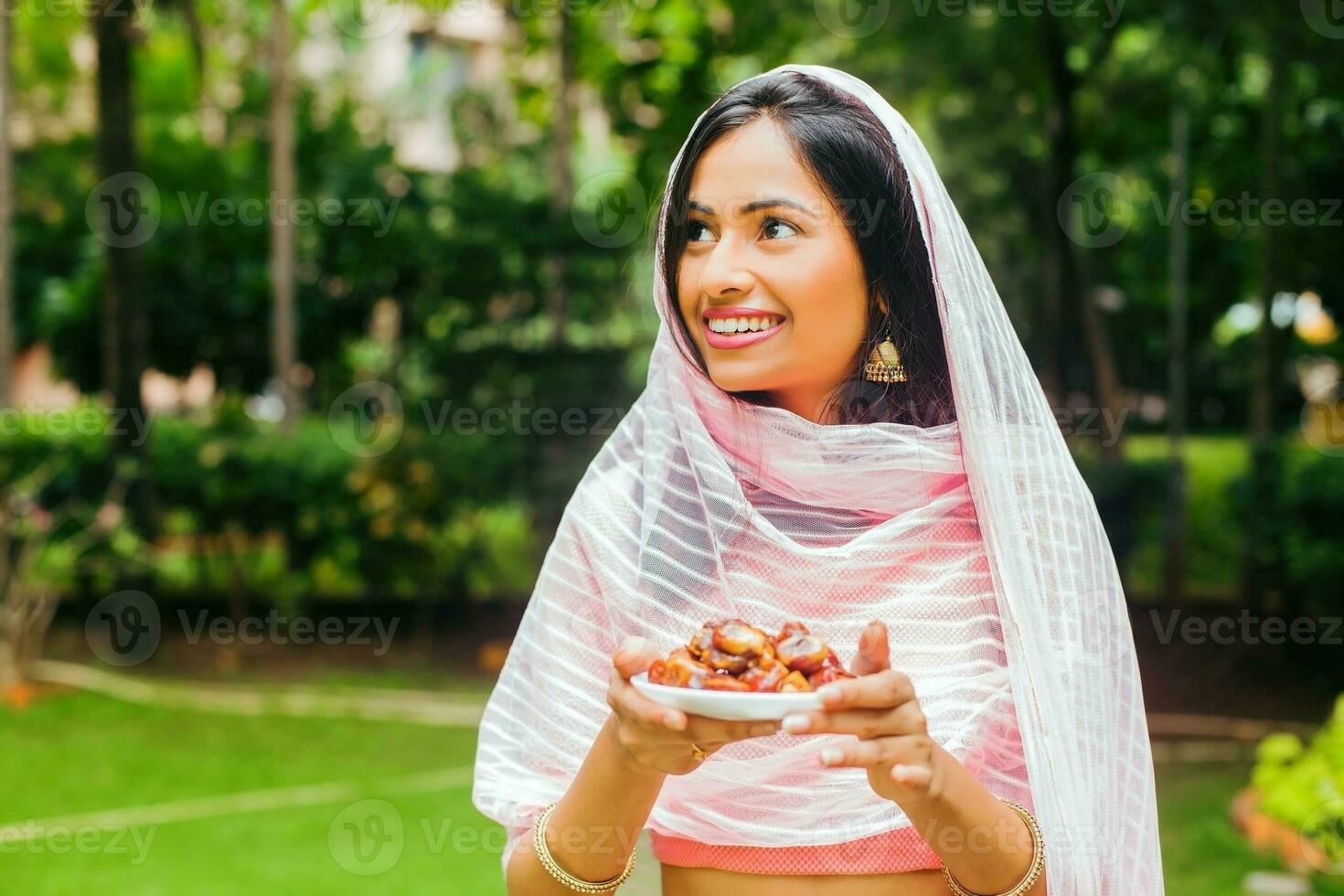 young beautiful indian woman holding a plate full of dates in a park photo