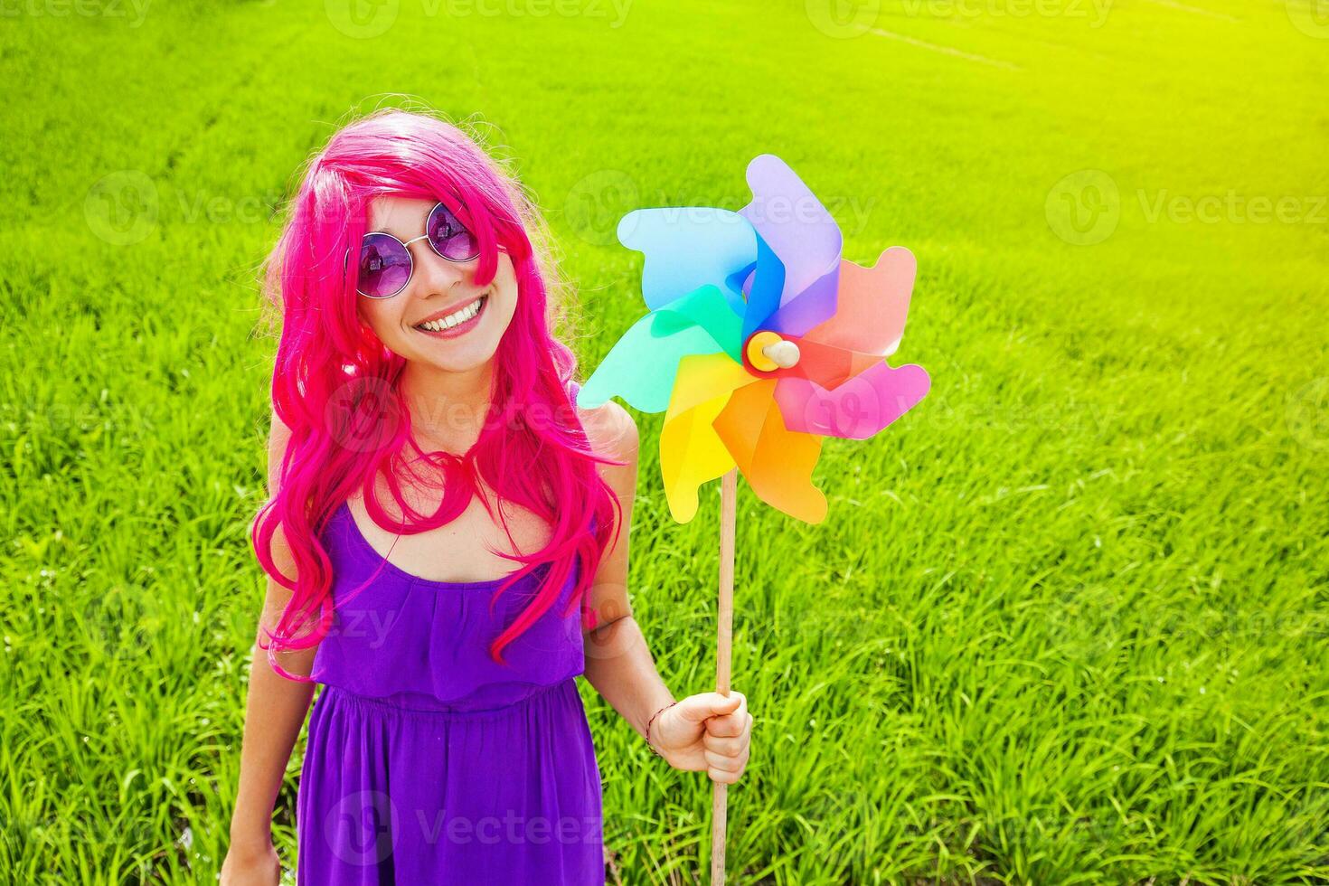 optimista joven mujer vistiendo rosado peluca posando al aire libre con molino foto