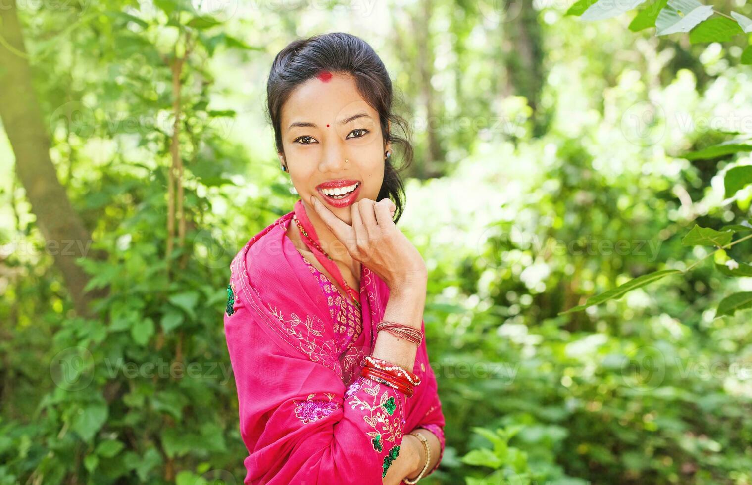 young beautiful nepalese woman wearing saree standing in a natural background of forest holding her hands by her face photo