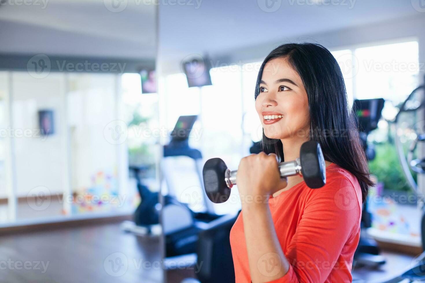 Pretty indonesian woman lifting weights in gym photo