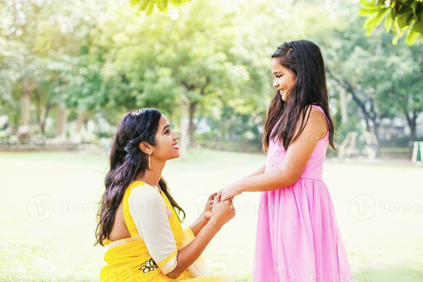 Cute Indian little girl and her mother holding hands and talking in the park photo