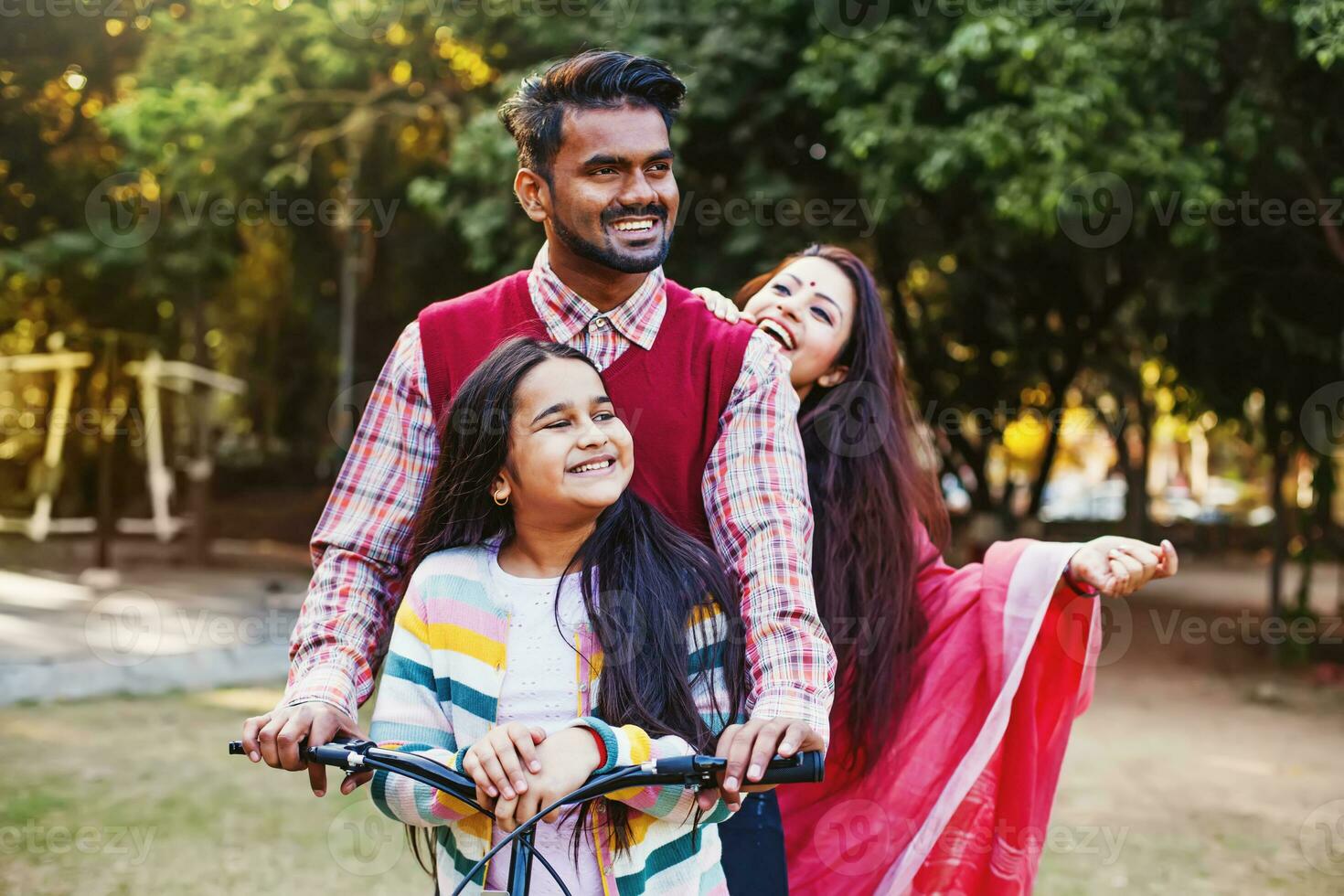 Beautiful Indian family - mother, father, daughter - riding a bicycle all together in the park photo