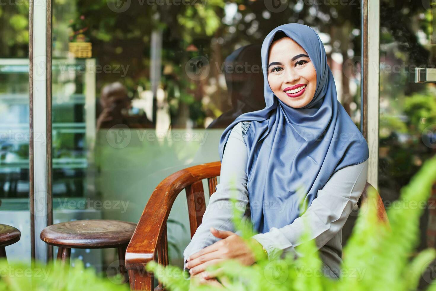 Beautiful Indonesian woman in her thirties sitting on a chair in a cafe, looking at camera and smiling photo