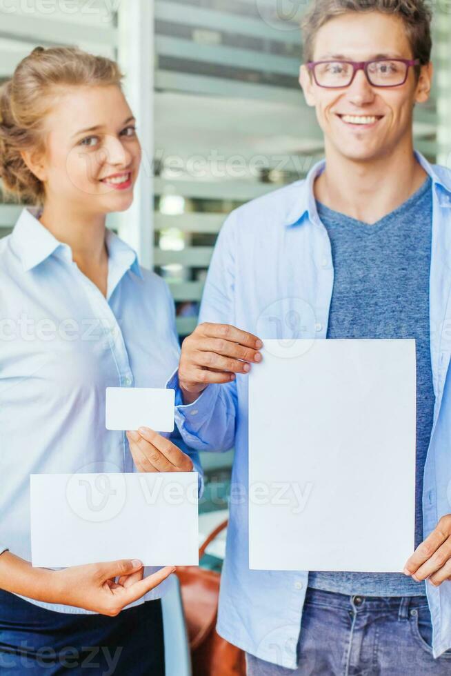 Blank name card, document template, envelope. Man and woman in office clothes holding elements of brand identity. Focus on documents photo