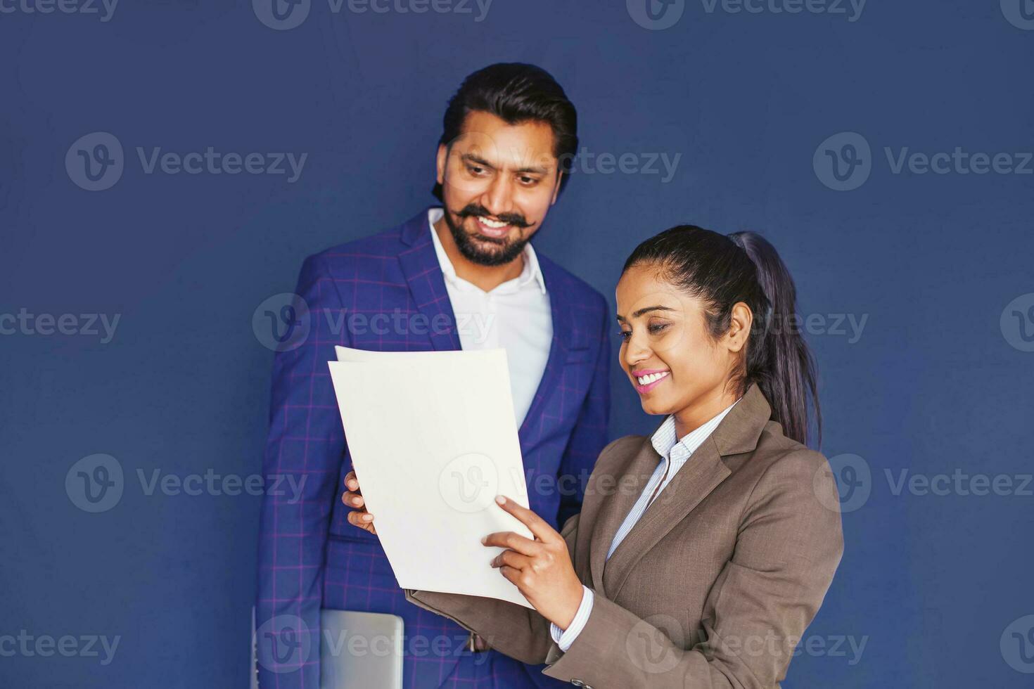 Young Indian female professional explaining contract details to tall Indian handsome man in business suit, isolated over blue studio background photo