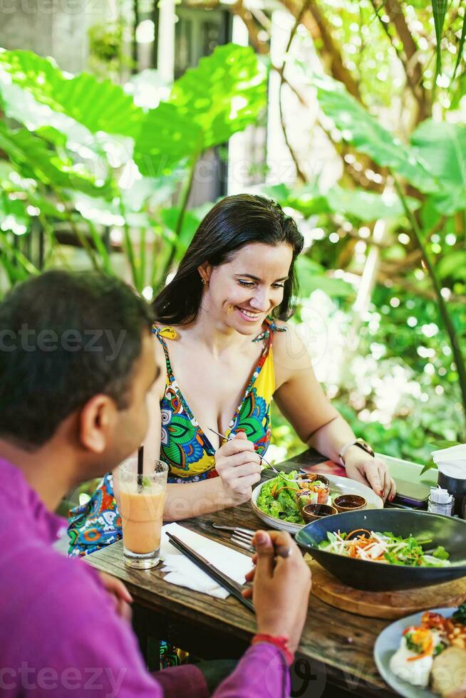 Happy couple in their 40s eating plant based food in outdoor restaurant in Bali, Indonesia photo