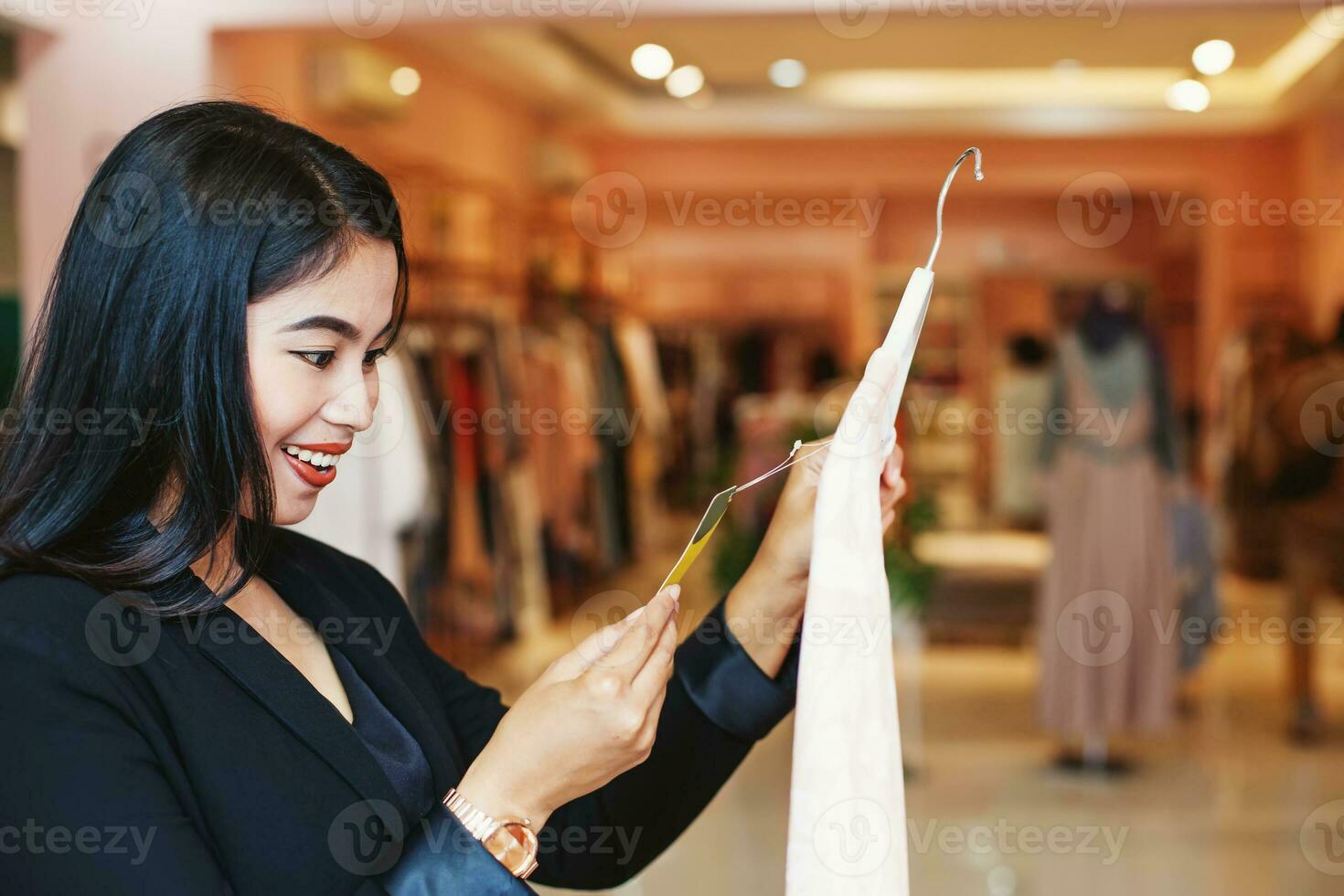 Asian woman looking at a price tag of a dress in a clothes store photo