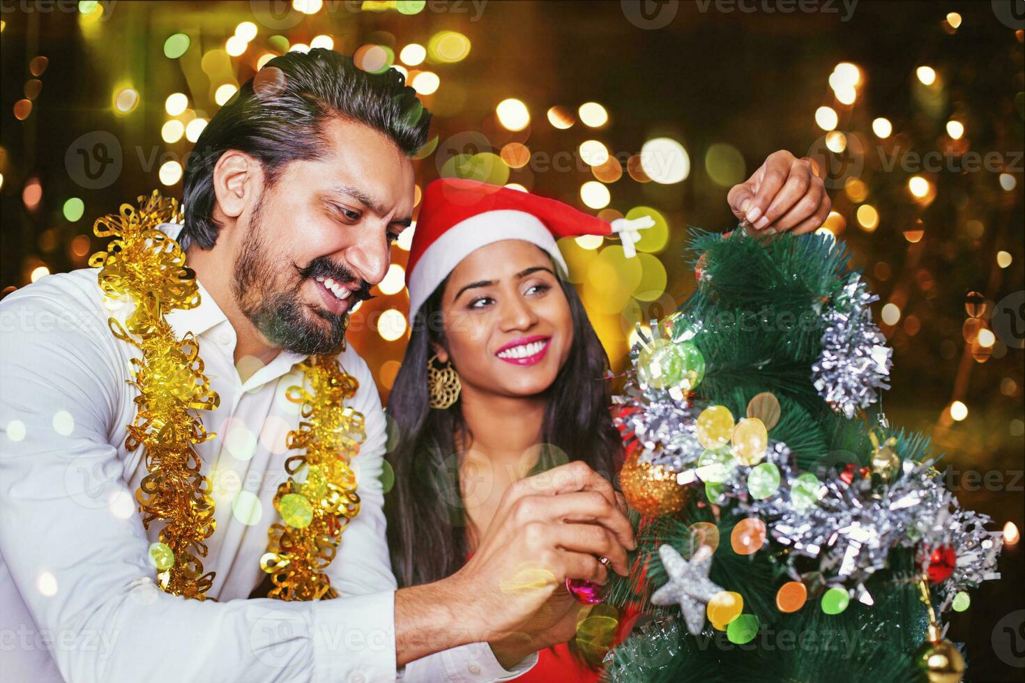 Beautiful Indian couple decorating Christmas tree with lights bokeh an the background photo